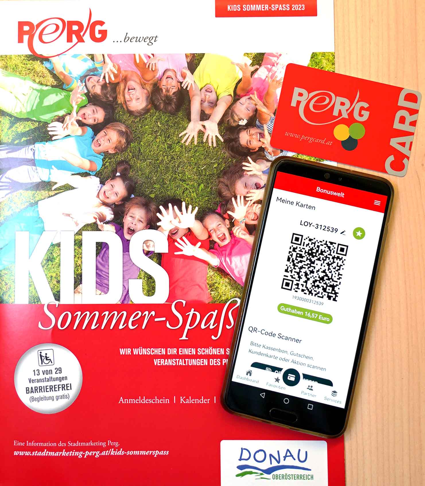 Programmheft KIDS Sommerspaß 2023 mit PERG-Card und auf dem Smart-Phone geöffneter PERG-Card-App